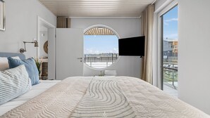 Un dormitorio con una cama grande, un ventanal redondo, un televisor de pantalla plana y vistas de la ciudad.