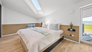 Un dormitorio moderno con tragaluces, una cama con colcha estampada y vista al mar a través de una puerta de vidrio.