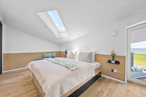 Ein modernes Schlafzimmer mit Dachfenster, einem Bett mit gemustertem Überwurf und Meerblick durch eine Glastür.