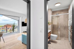 Een moderne badkamer met douche, toilet en een groot raam met uitzicht op zee.