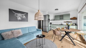 Una sala de estar moderna con un sofá azul, una mesa de centro redonda y un comedor con una mesa y sillas de madera.