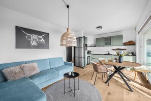 Ein modernes Wohnzimmer mit einem blauen Sofa, einem runden Couchtisch und einem Essbereich mit einem Holztisch und Stühlen.