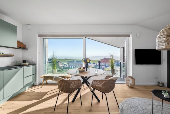 Een moderne woonruimte met een grote schuifpui naar een balkon, een eethoek met een ronde tafel en een keuken met een groen kastje.