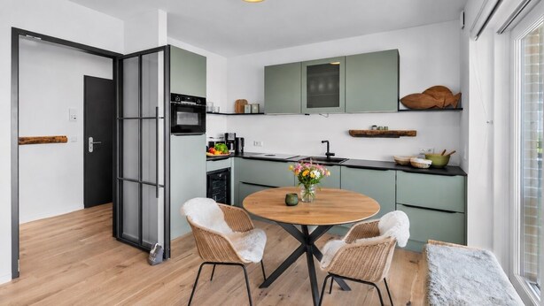 Una cocina moderna con comedor, que incluye una mesa redonda, dos sillas y un jarrón con flores.