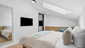 Une chambre moderne avec un plafond en pente, un lit recouvert d’une housse matelassée, un téléviseur à écran plat et un grand miroir.
