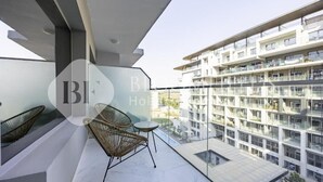 Varanda de hotel moderna com cadeiras de vime e uma pequena mesa, com vista para um edifício alto.