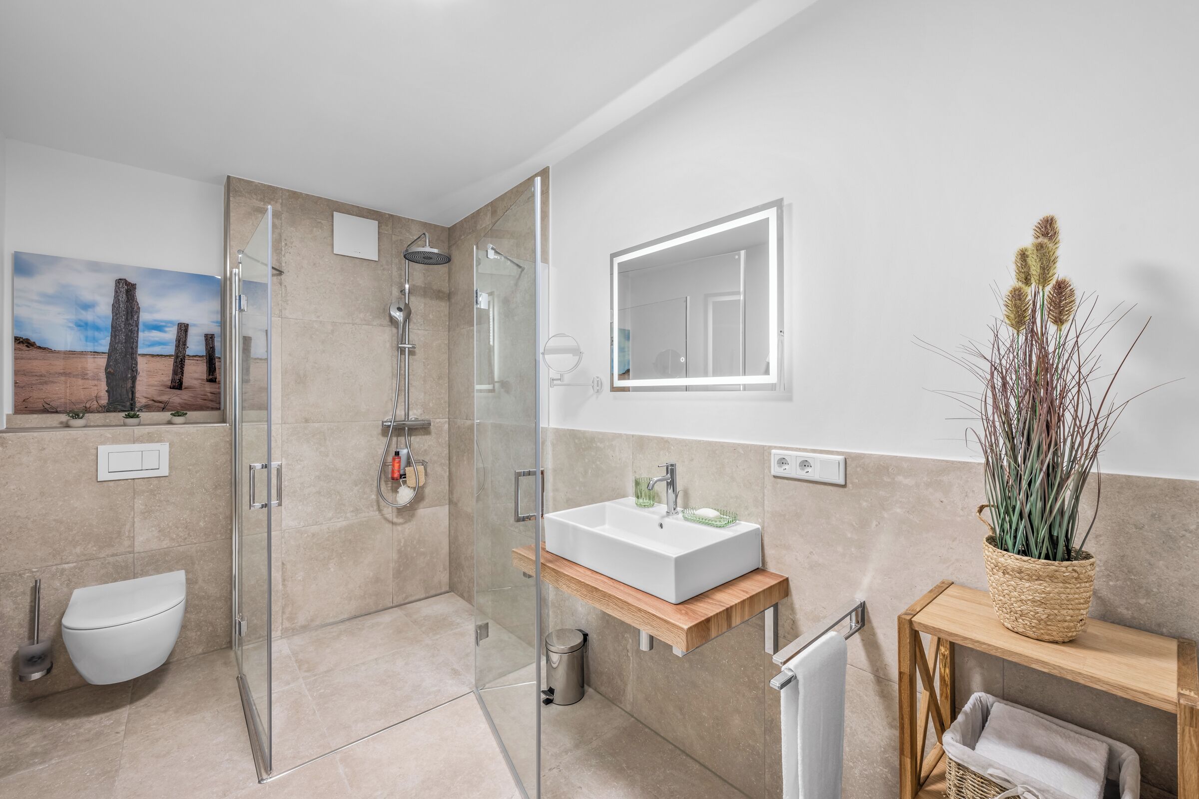 Een moderne badkamer met een douchecabine van glas, een wit wastafeltje en een houten opbergmeubel.