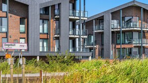 A modern multi-story building with a mix of brick and glass facades, balconies, and a clear sky. - The View B08 Kapitänskajüte - Elevator, shared Sauna, underfloor heating,balcony (Dagebüll)