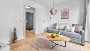 A modern living room with a grey sofa, a wooden coffee table with fruit, a hanging pendant light, and a framed artwork on the wall. - The View B08 Kapitänskajüte - Elevator, shared Sauna, underfloor heating,balcony (Dagebüll)
