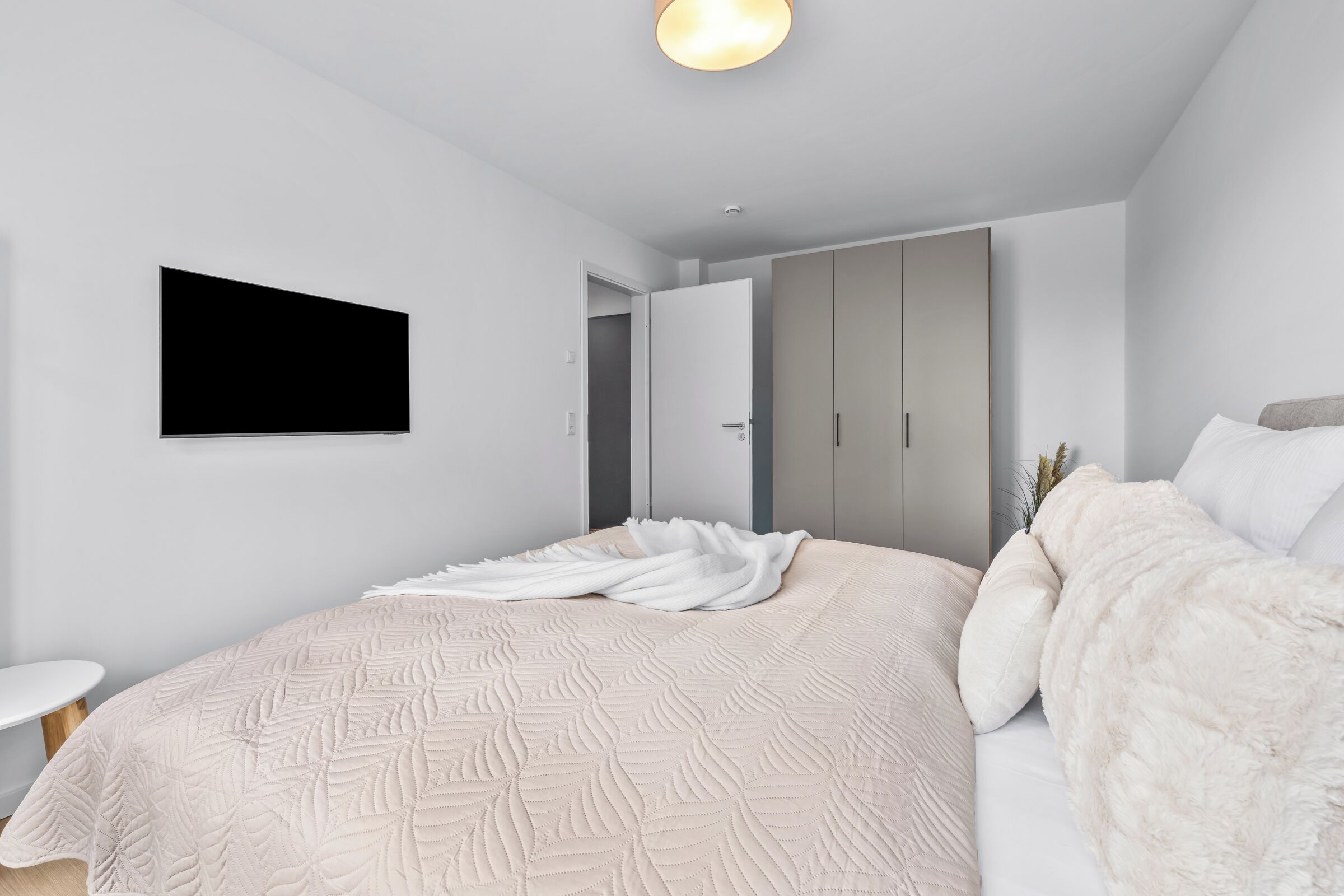 Una camera da letto moderna con un letto grande, una TV a schermo piatto montata a parete e un armadio con ante scorrevoli.