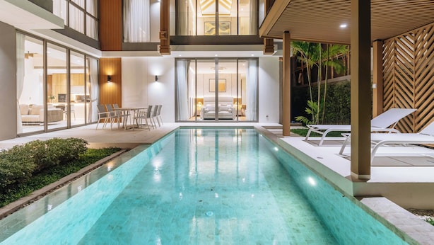 Ein moderner, überdachter Pool mit Glaswänden, eine Lounge mit Sesseln und Blick auf den Pool.