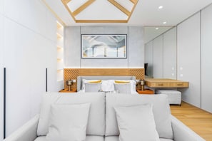 A modern hotel room with a large bed, a sofa, a wooden bedside table, a TV, and a large mirror. - Brand New 3Br Elite Pool Villa V293 (Choeng Thale)