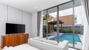 Ein modernes Schlafzimmer mit einem großen Bett, einem Fernseher auf einer Holzkommode und Blick auf einen Swimmingpool und Außenbereich.