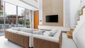 Ein modernes Wohnzimmer mit einem großen Ecksofa, einem Flachbildfernseher, der an einer Holzwand angebracht ist, und einer Treppe mit Holzbodenstufen.