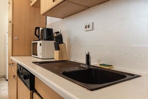 A kitchen with a black sink, a white microwave, a coffee maker, and wooden cabinets. - Comfy Room Long Stay Near Belvedere (Vienna)