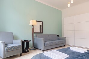 A hotel room with a sofa, a chair, a lamp, a bed, and a wardrobe. - Comfy Room Long Stay Near Belvedere (Vienna)