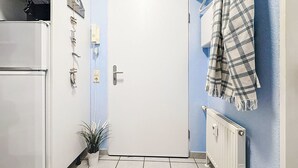 Una cucina compatta con un frigorifero bianco, una porta bianca, una piccola pianta in vaso e un termosifone.