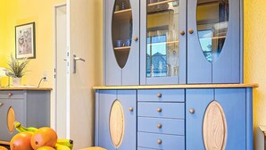 Una stanza con un armadio blu dotato di vetrate, un tavolo di legno con una ciotola di frutta e un piccolo oggetto decorativo.