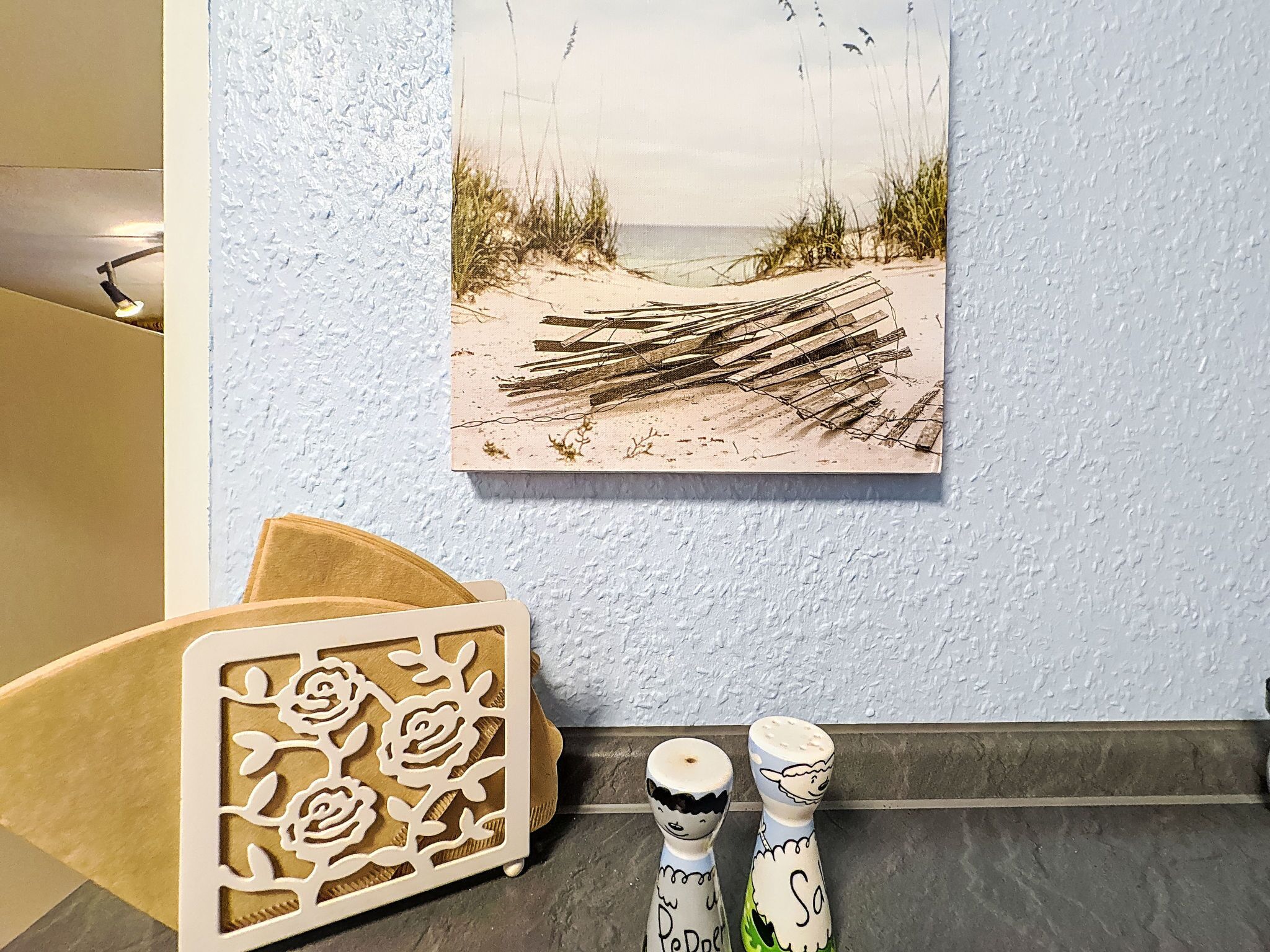 A wall with a beach painting, a decorative wooden panel, and two salt and pepper shakers.