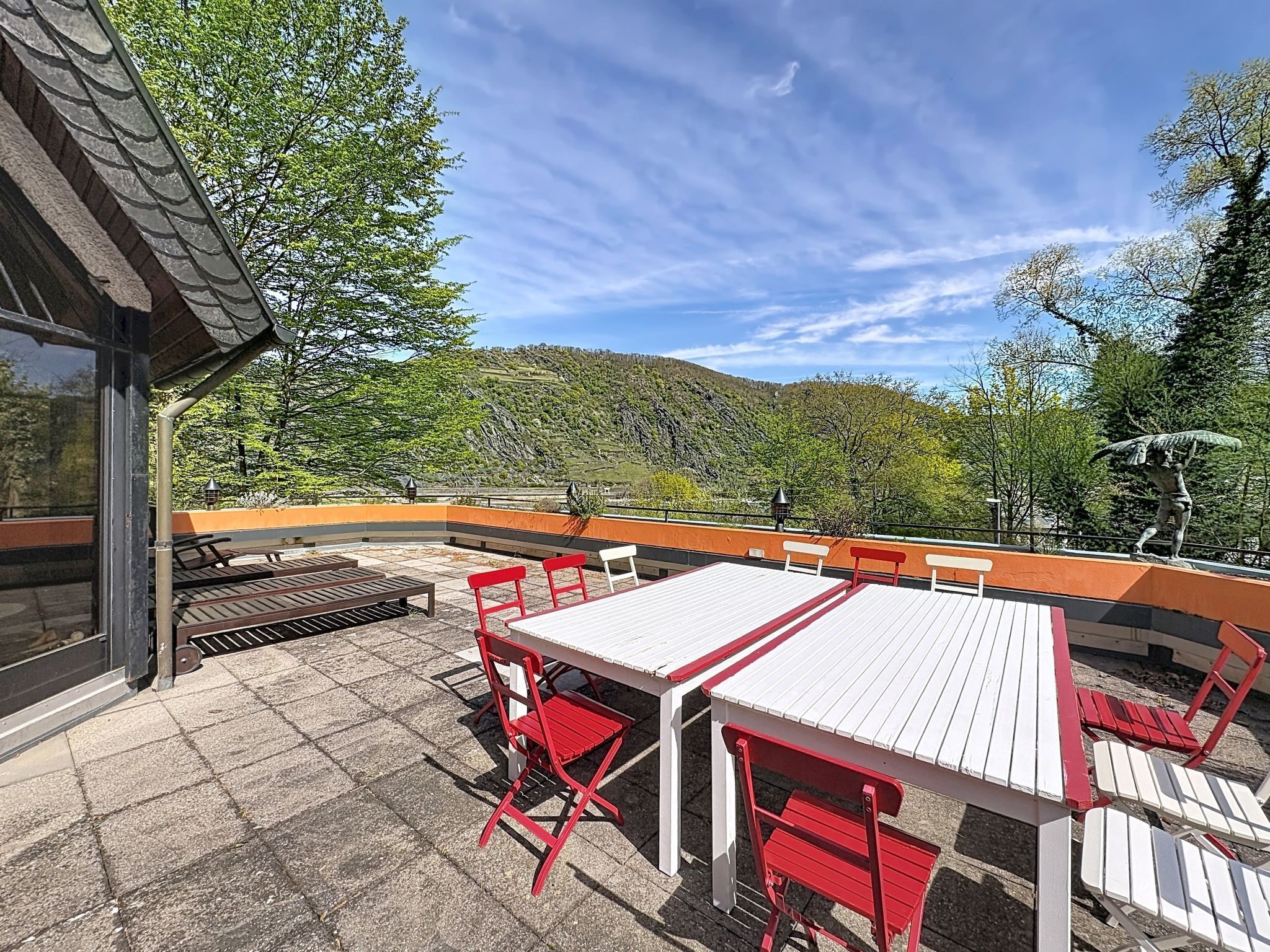 An outdoor patio with a table and chairs, a view of a hillside, and a statue.