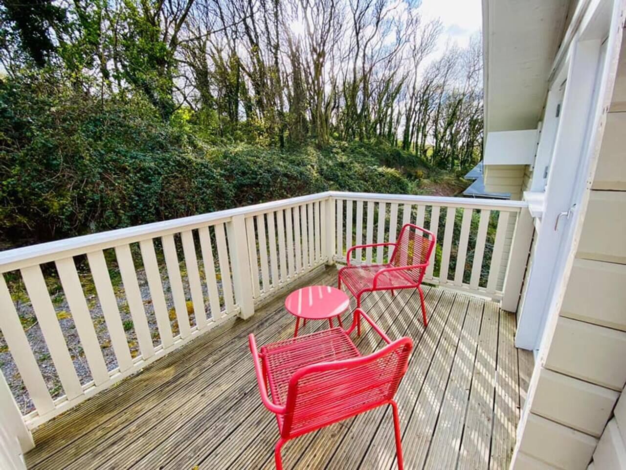 Une terrasse en bois avec une balustrade blanche, deux chaises rouges et une petite table ronde.