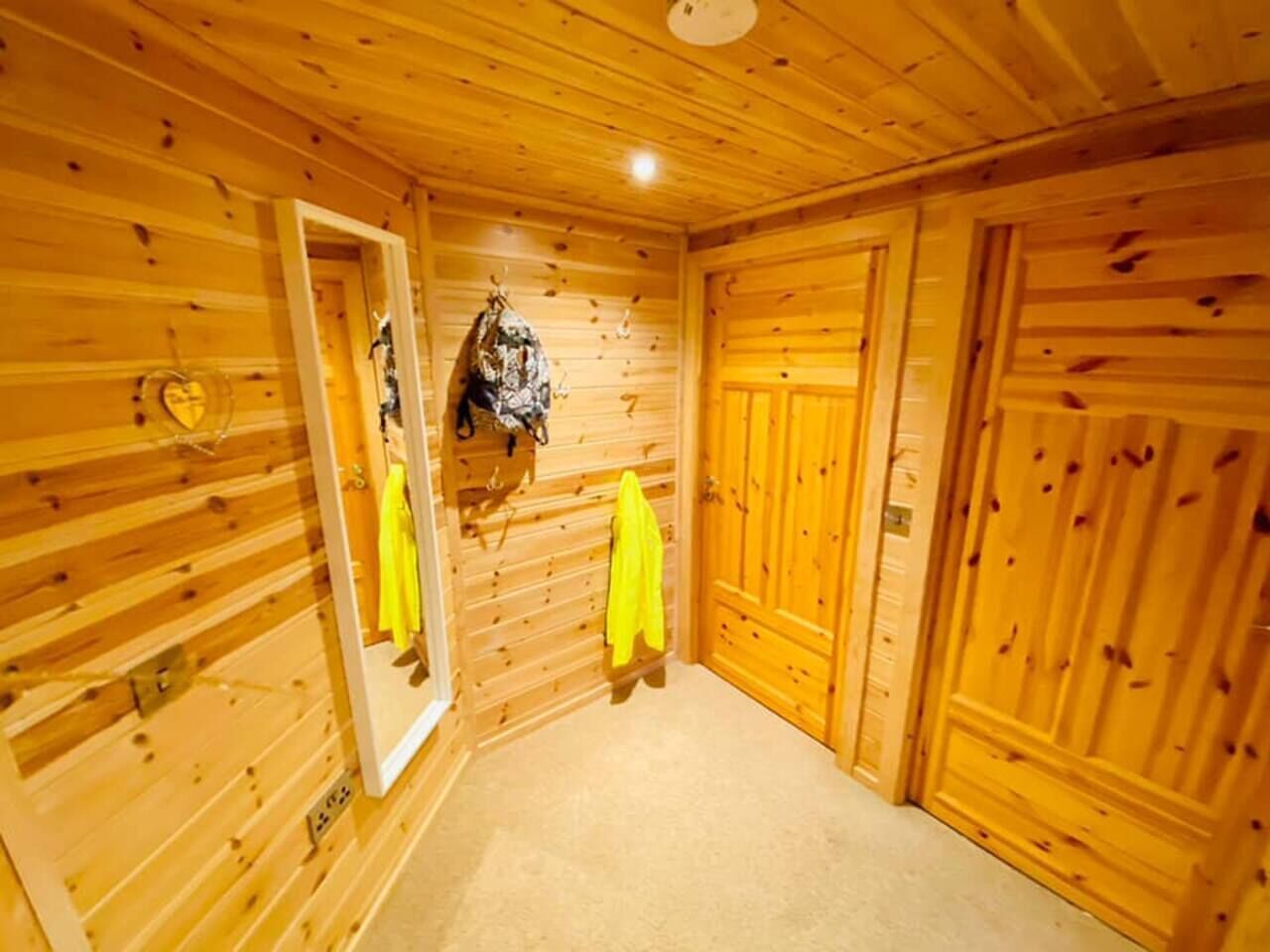 Quarto com painéis de madeira, uma porta, um cabideiro com um casaco e um espelho.