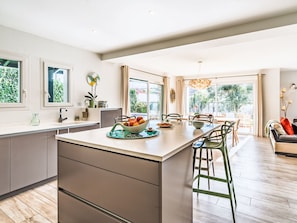 A modern kitchen with a central island, bar stools, and a dining area with a view of the outdoors. - Xoxotartea by Interhome (Saint Pée sur Nivelle)