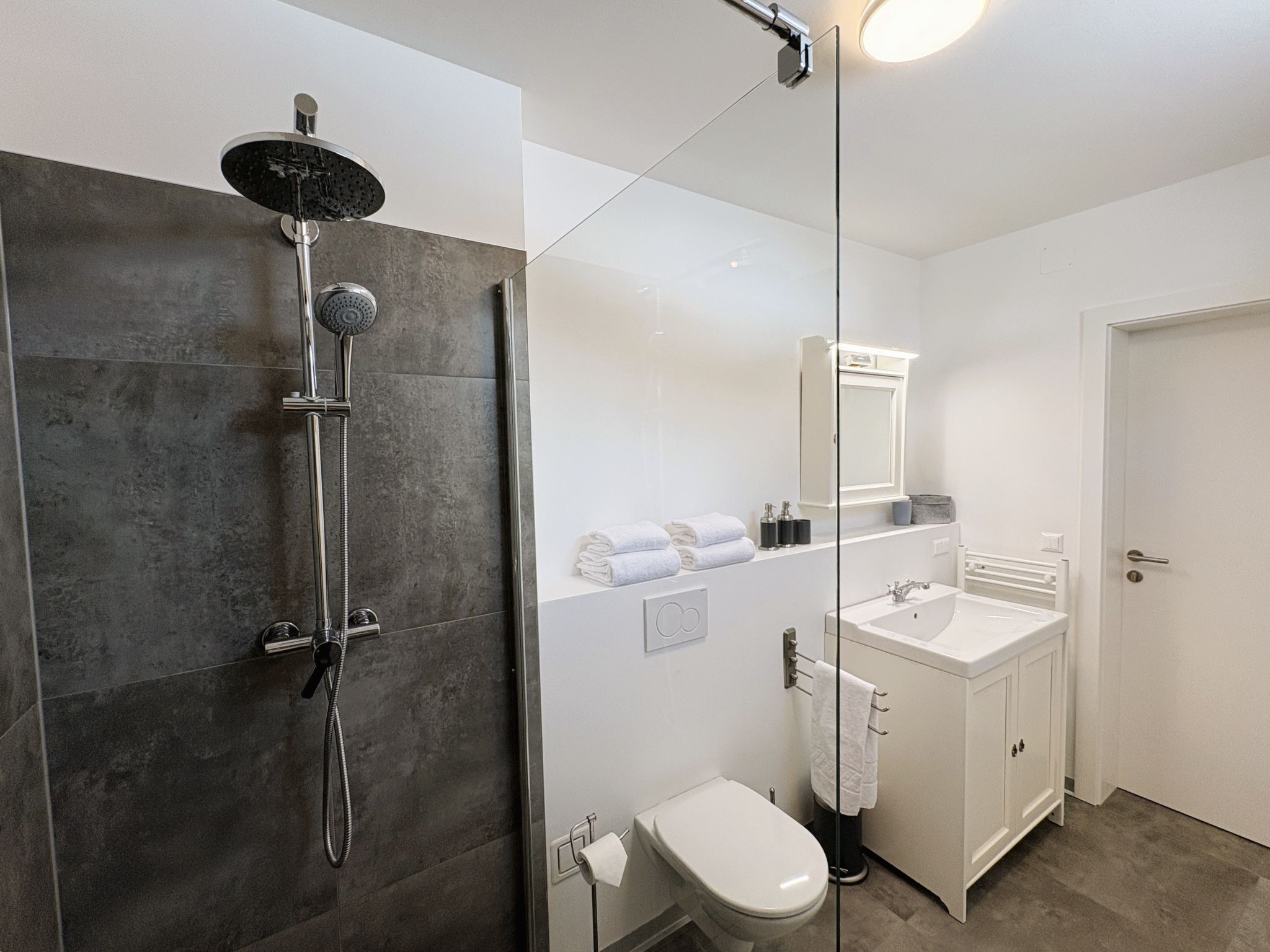 Ein modernes Badezimmer mit Dusche, Toilette, Waschbecken und Spiegel.
