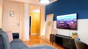 Un salon comprenant un canapé, un téléviseur fixé au mur, une cheminée et une porte donnant sur une autre pièce.
