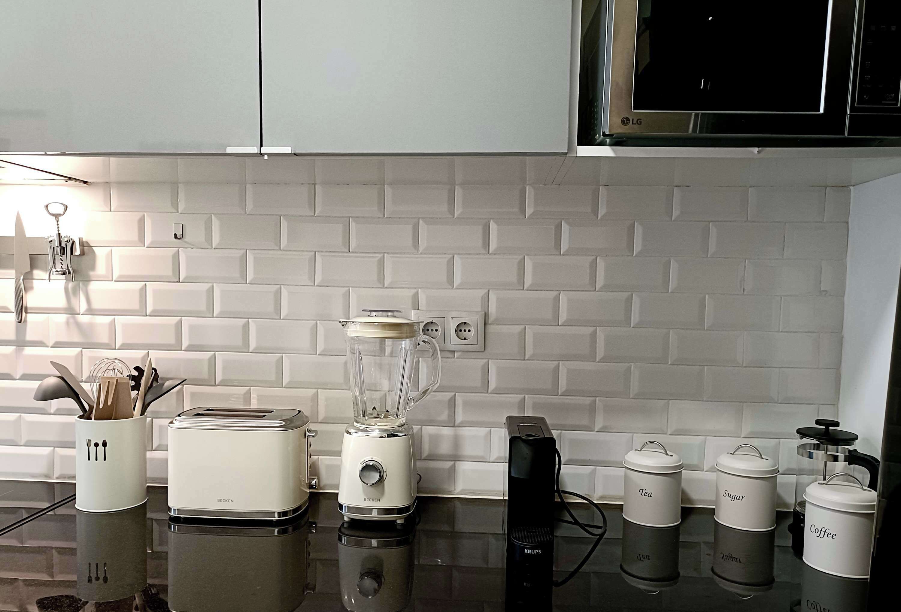A kitchen with white tiled backsplash, a toaster, a blender, and storage containers labeled tea, sugar, and coffee.