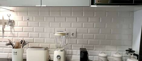 A kitchen with white tiled backsplash, a toaster, a blender, and storage containers labeled tea, sugar, and coffee.