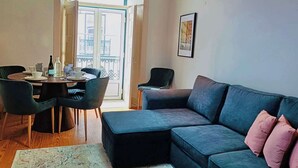 Un salon moderne avec un canapé gris foncé, un petit pouf et un coin repas avec une table mise pour deux personnes.