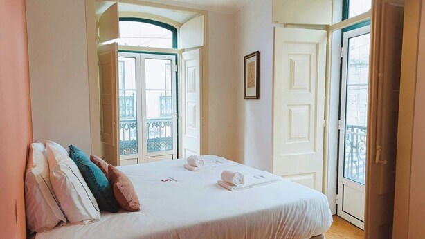 Une chambre d’hôtel avec un lit, une table de chevet, une lampe et une fenêtre donnant sur un balcon.
