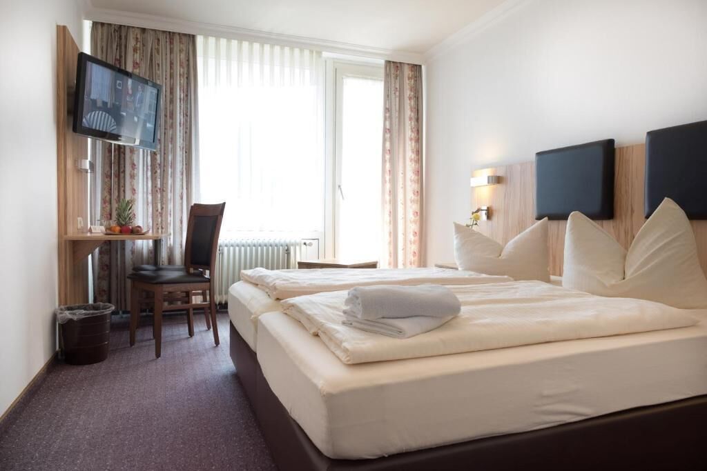A hotel room with two beds, a desk with a chair, a television, and a window with curtains.