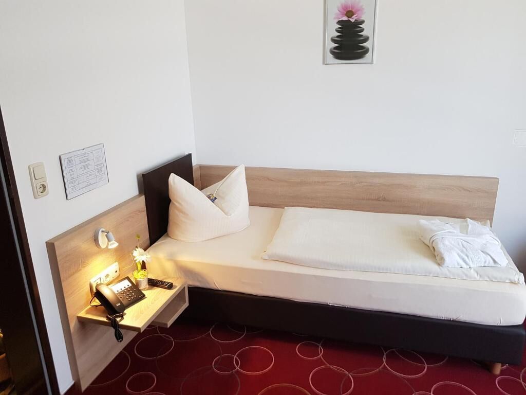 Ein Hotelzimmer mit einem Bett, einem Nachttisch mit Telefon und Lampe, einer an der Wand befestigten Speisekarte und einem gerahmten Kunstwerk über dem Bett.