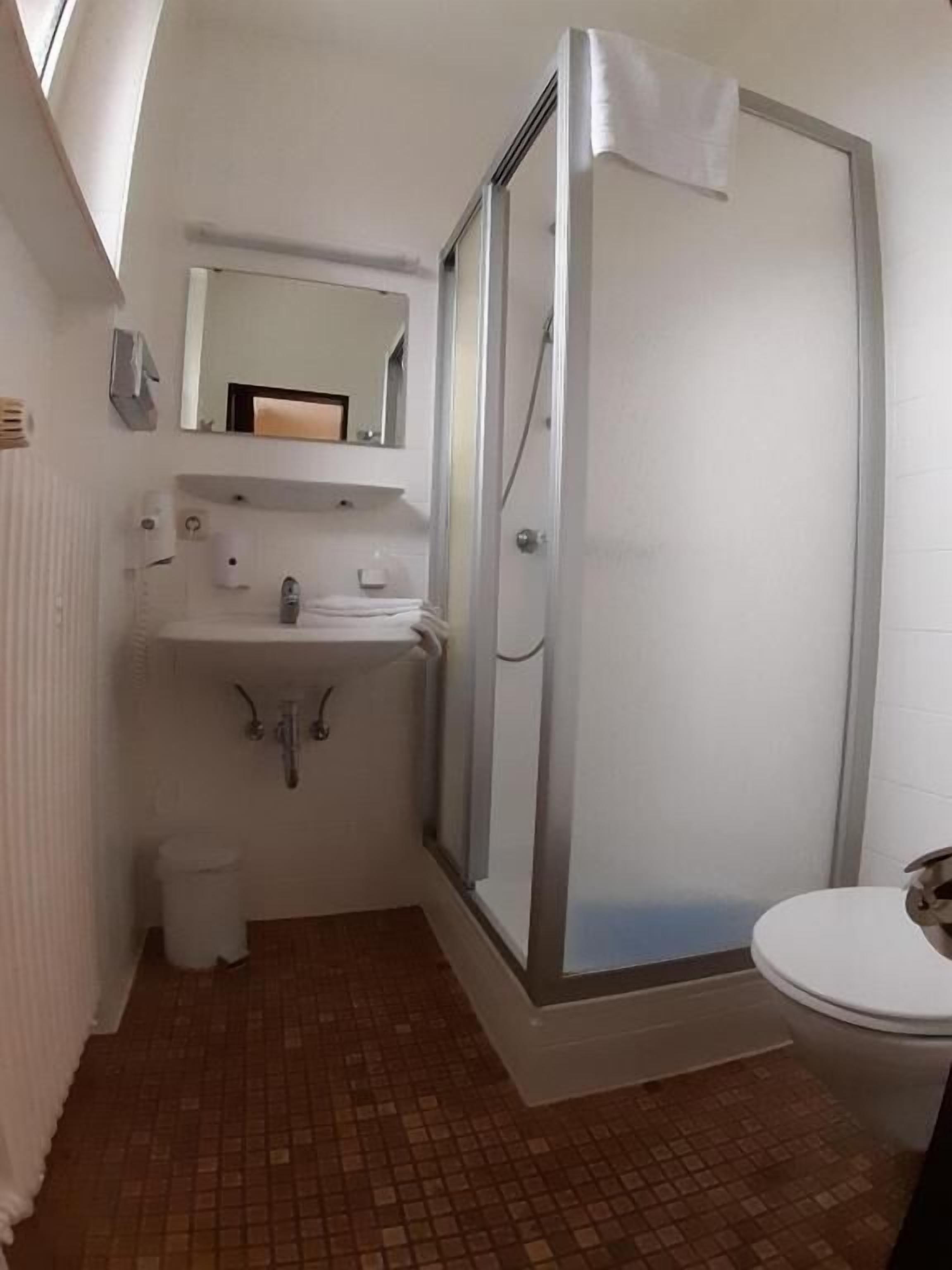 A compact bathroom with a shower enclosure, a toilet, and a sink with a mirror above it.