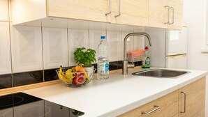 Cuina amb armaris blancs, un rentamengesines d'acer inoxidable, un cesto de fruita amb plàtans i pomes, una ampolla d'aigua i una ampolla de sabó per a plats.
