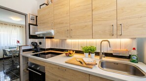 A modern kitchen with wooden cabinets, a stainless steel sink, and a countertop with a fruit bowl and potted plants. - Central Vecindario Apartment · 10 min from Airport · Fast WiFi (Vecindario)