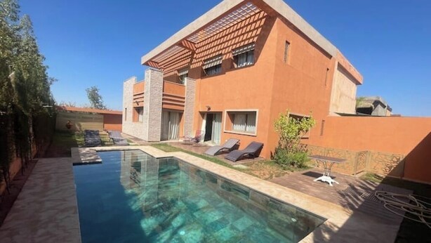 Ein modernes Haus mit Swimmingpool, einer Terrasse mit Liegestühlen und einem Garten.