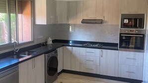 Eine moderne Küche mit hellen Holzschränken, einer schwarzen Arbeitsplatte, einem eingebauten Backofen und einer Waschmaschine.