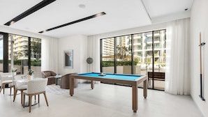 A modern living room with a pool table, a dining area, and large windows offering a view of the surrounding buildings. - Stayshort - 1 Bed That Sleeps 4 With Amazing Beach View (Dubai)