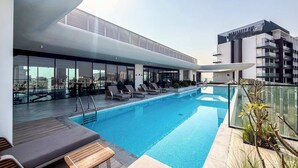 Ett modernt poolområde på taket med solstolar och en fri utsikt över stadsbilden.