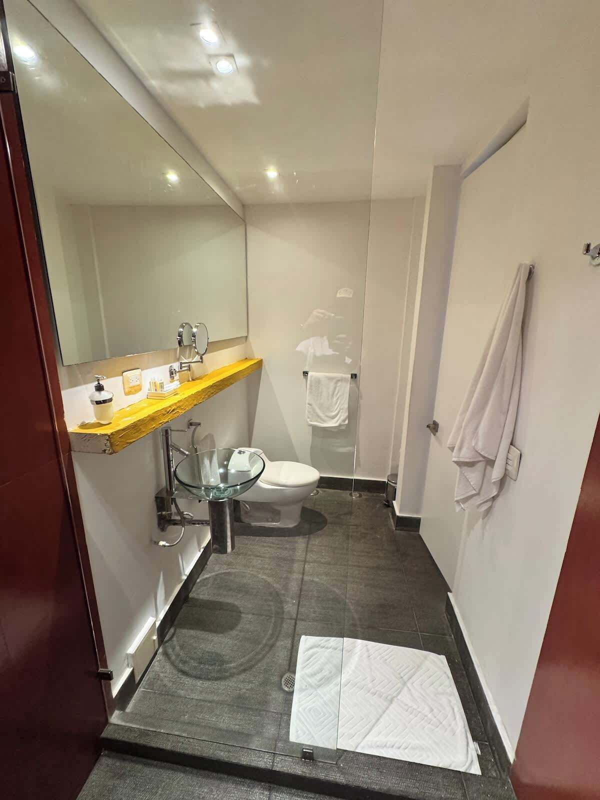 A compact bathroom with a glass shower enclosure, a white toilet, and a wooden vanity with a mirror.