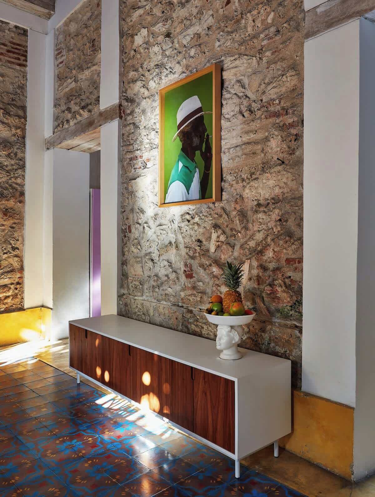 A lobby with a stone wall, a framed picture, a white console table, and a fruit bowl.
