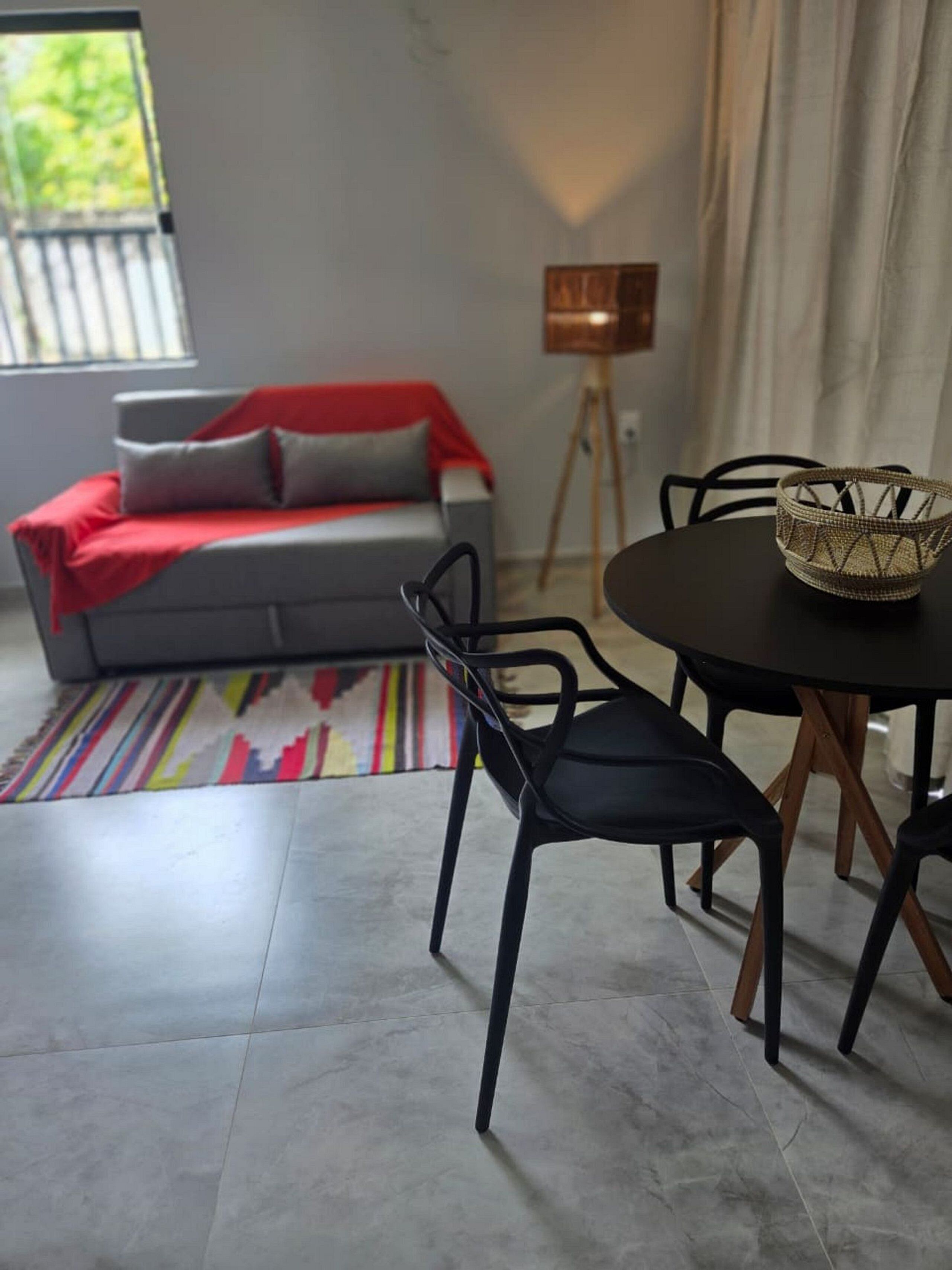Una sala de estar moderna con un sofá gris, sillas negras, una mesa redonda y una alfombra colorida.