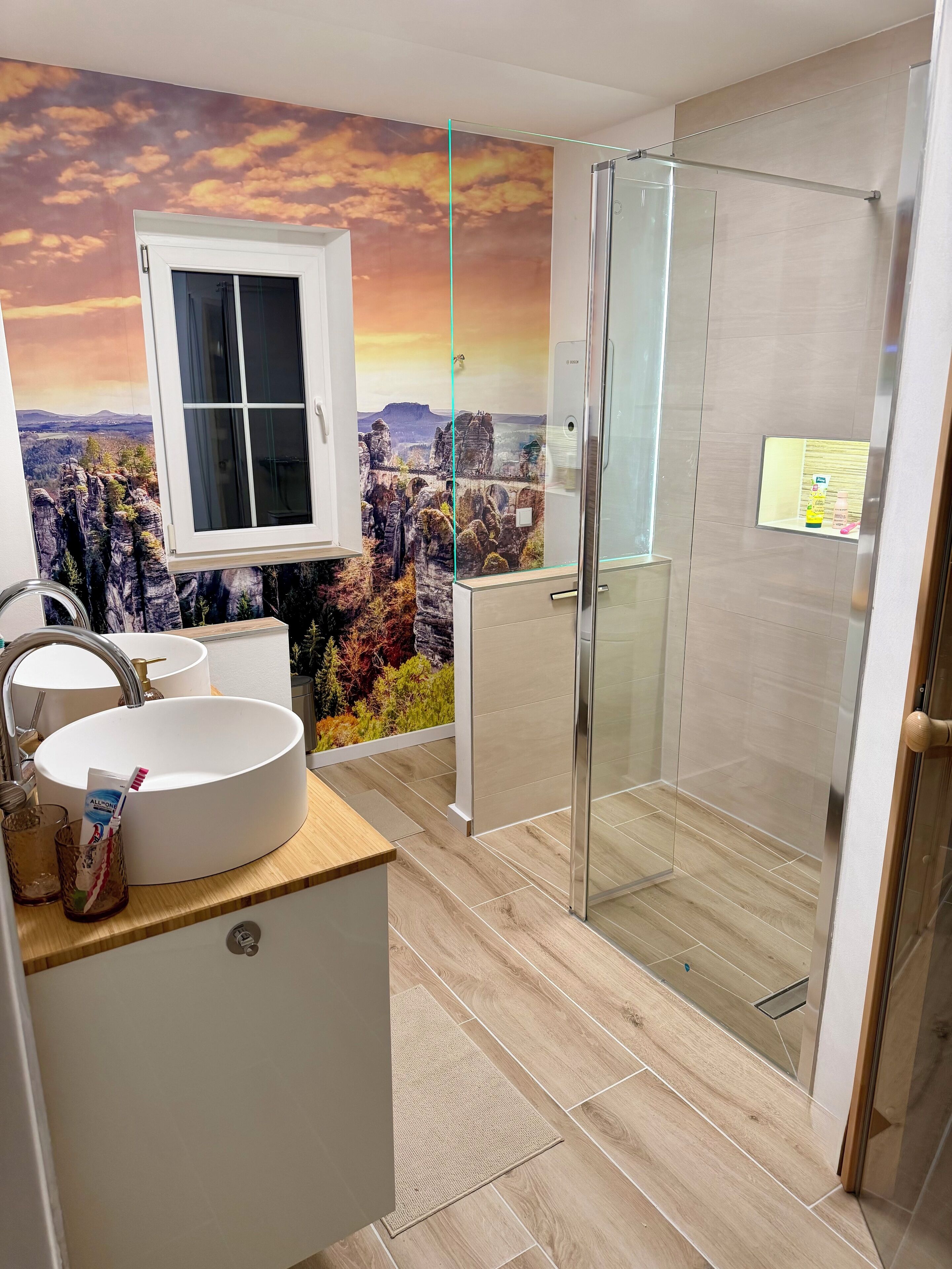 Un baño moderno con un lavamanos grande, una cabina de ducha de vidrio y un mural decorativo en la pared.