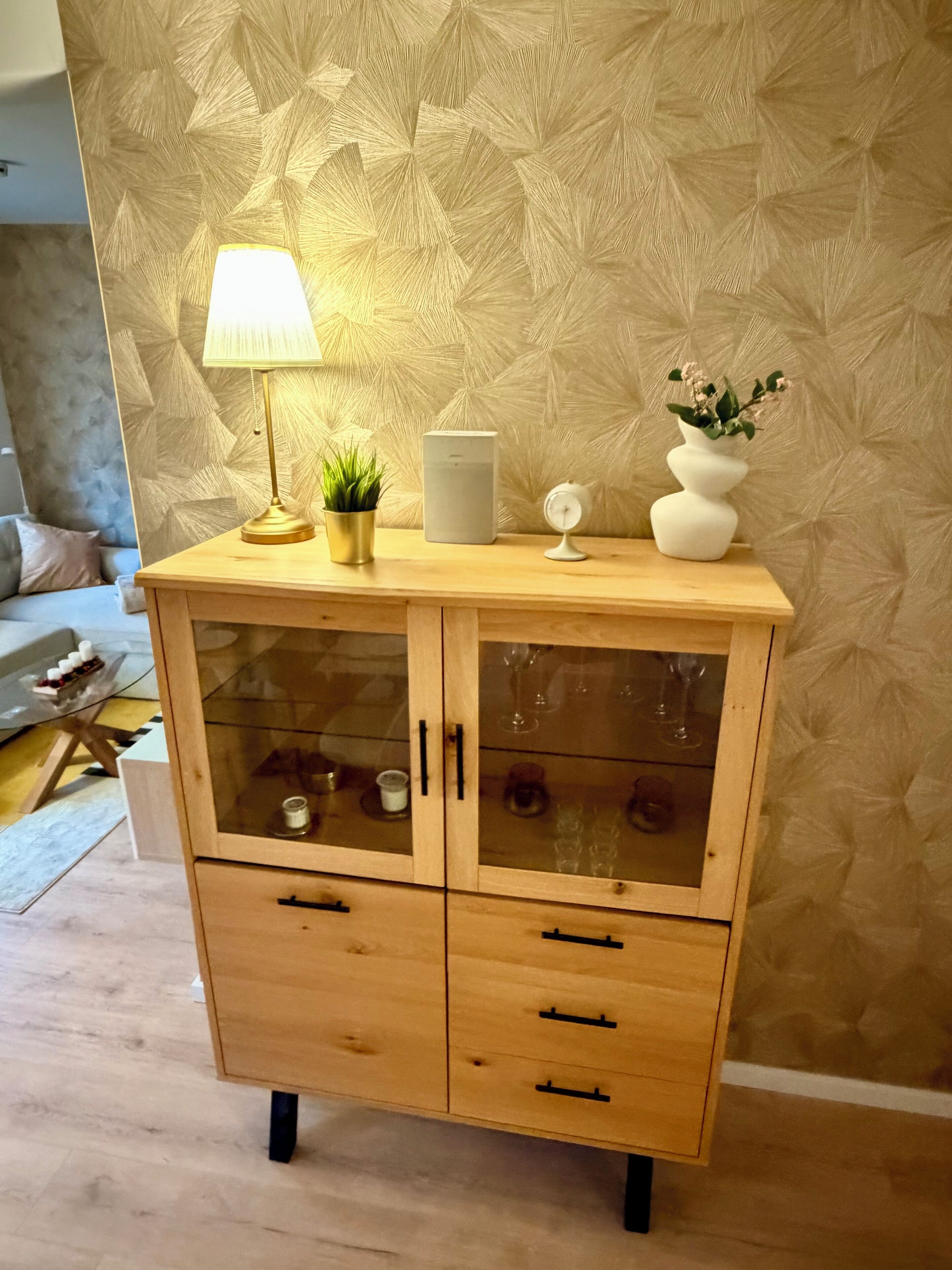 A wooden cabinet with glass doors, a lamp, a potted plant, a white vase with flowers, and a white clock.