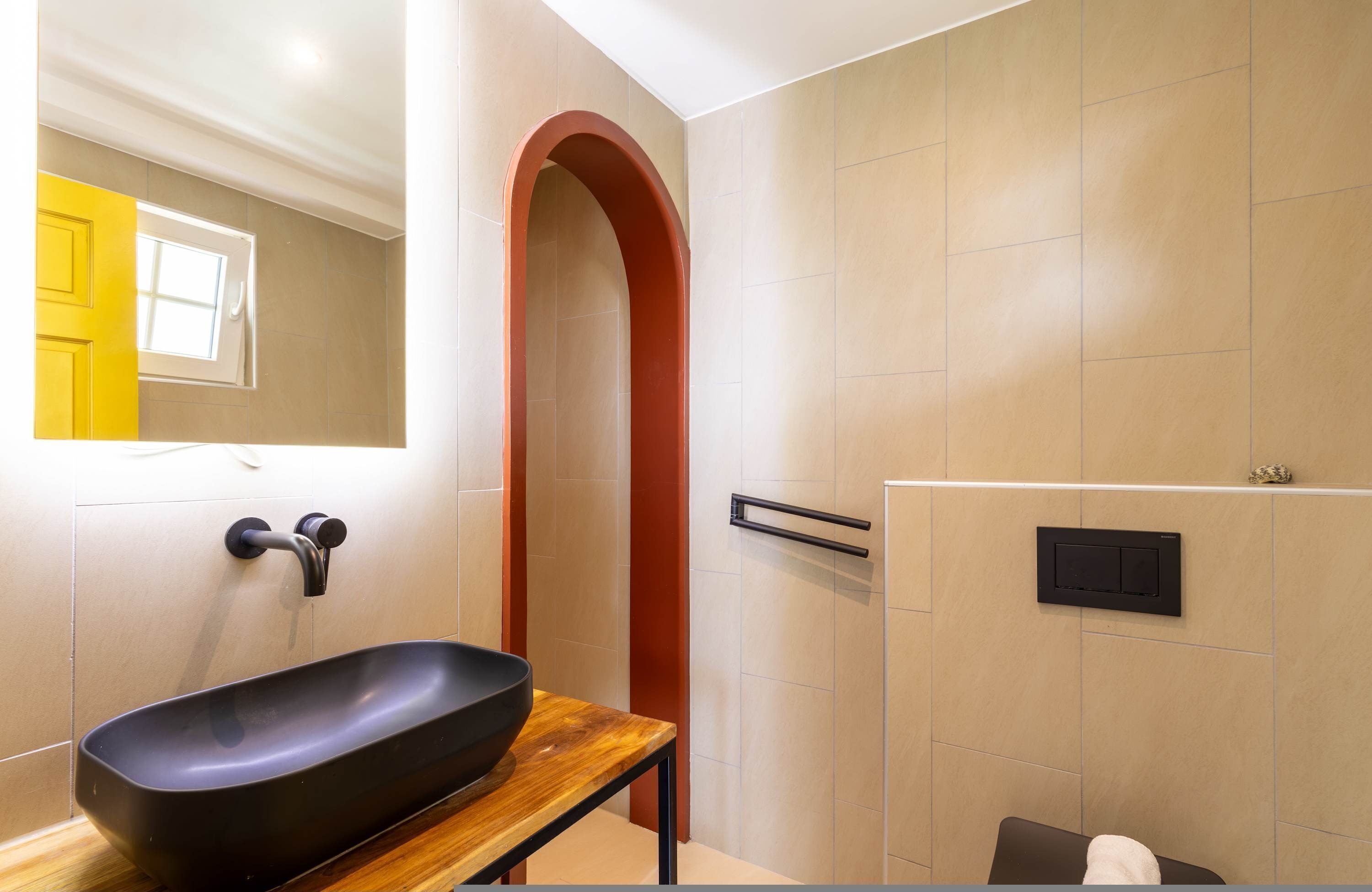 A modern bathroom with a black basin, a wooden countertop, a towel rack, and a shower control panel.