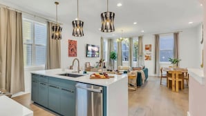 A modern kitchen with a central island, a dining area with a wooden table, and a living space with a sofa and a coffee table. - Hip Rooftop Deck Game Room in Downtown Nashville (Nashville)