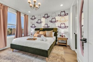 Ein Schlafzimmer mit einem großen Bett, einer Kronleuchter, einer Wand mit Hutmotiven und Blick ins Freie.